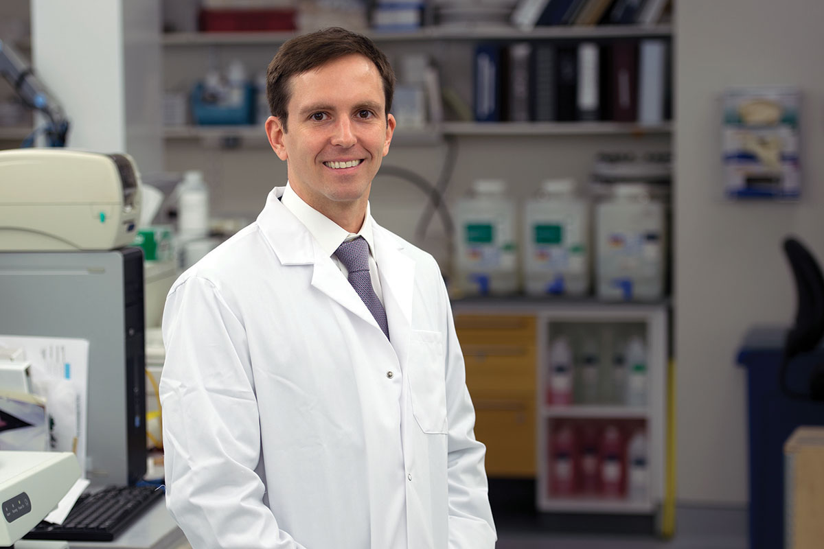 Travis Hollmann in a white coat in his laboratory