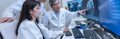Radiation oncologist Dr. Nancy Lee, medical oncologist Dr. Alan Ho, and surgeon Dr. Richard Wong look at scans on computer monitors.